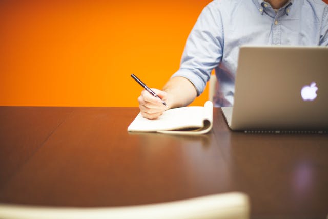person writing notes while looking at something on their laptop