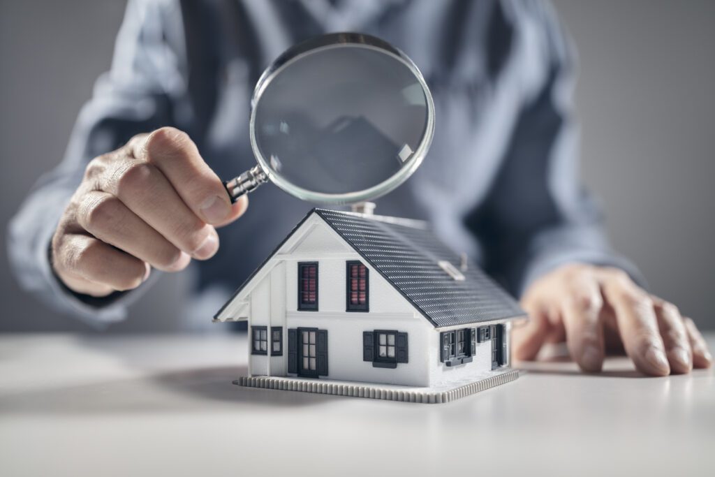 person holding a magnifying glass over a home figurine