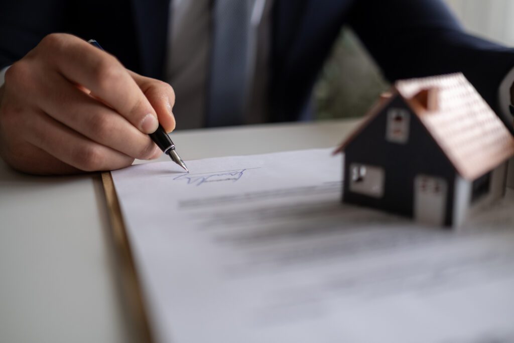 a person signing a document with a house figurine one it