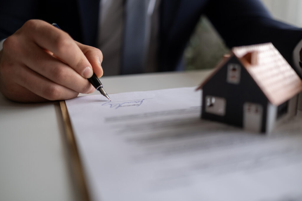 person signing a document with a house figurine