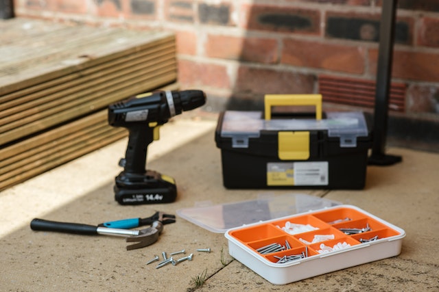 drill, tool box, box of screws and nails and a hammer on sidewalk